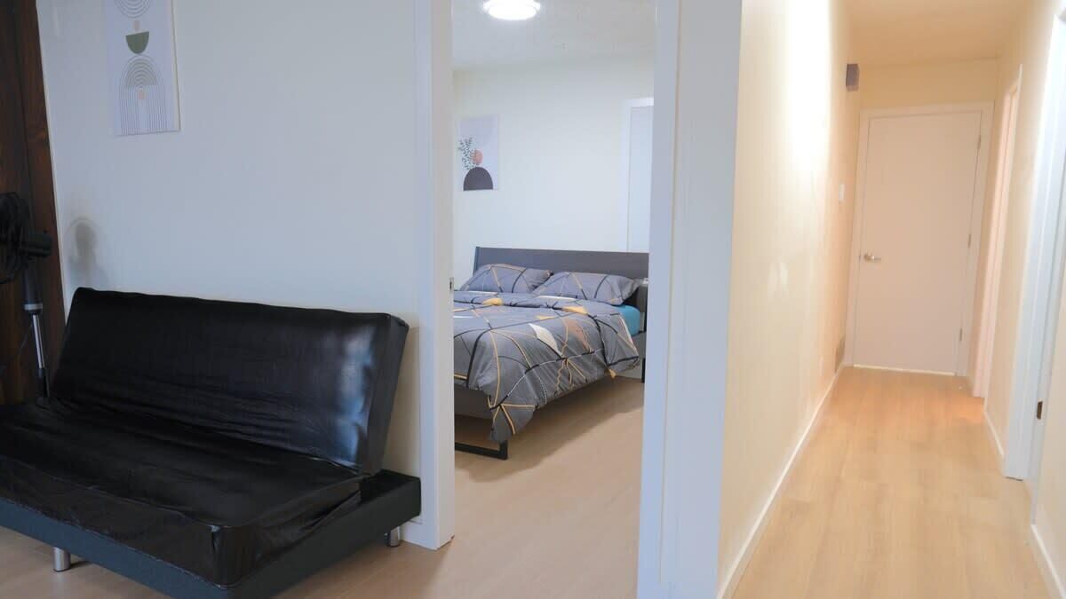 A room with a black leather sofa, a bed with patterned bedding, a white door, and a wooden floor.