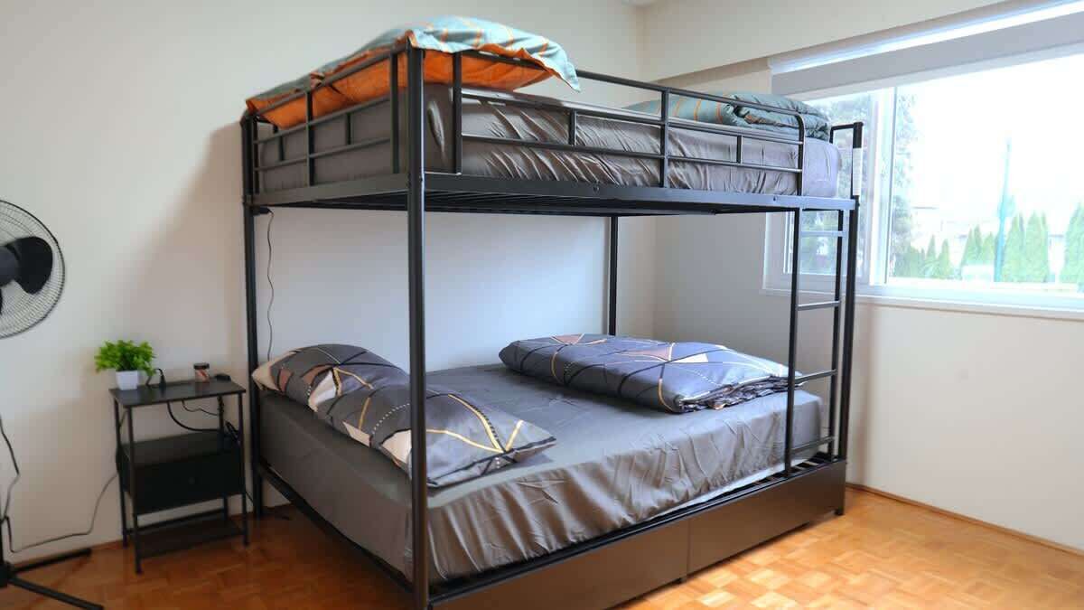 A bunk bed with a desk and chair, a small plant, and a window with a view of trees.