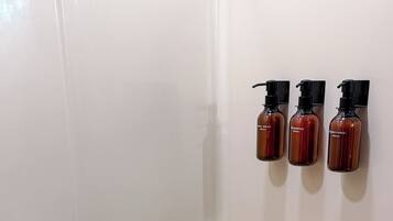 A white bathtub with a handrail and three bottles of shampoo and conditioner on the wall.