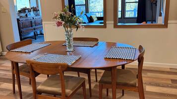 En matplats med ett träbord och stolar, en vas med blommor och utsikt över en balkong genom ett fönster.