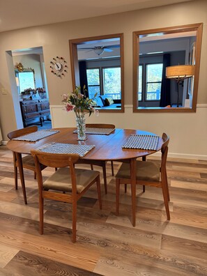A dining area with a wooden table and chairs, a vase with flowers, and a view of a balcony through a window. - Mountain Daddies Bed & Breakfast (Oakhurst)