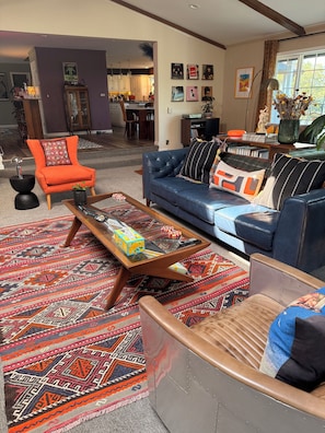 Una sala de estar moderna con un sofá azul, un sillón naranja y alfombras estampadas.