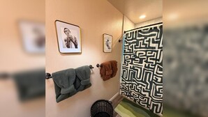 Un baño con cortina de ducha estampada, una toalla verde y dos cuadros en la pared.
