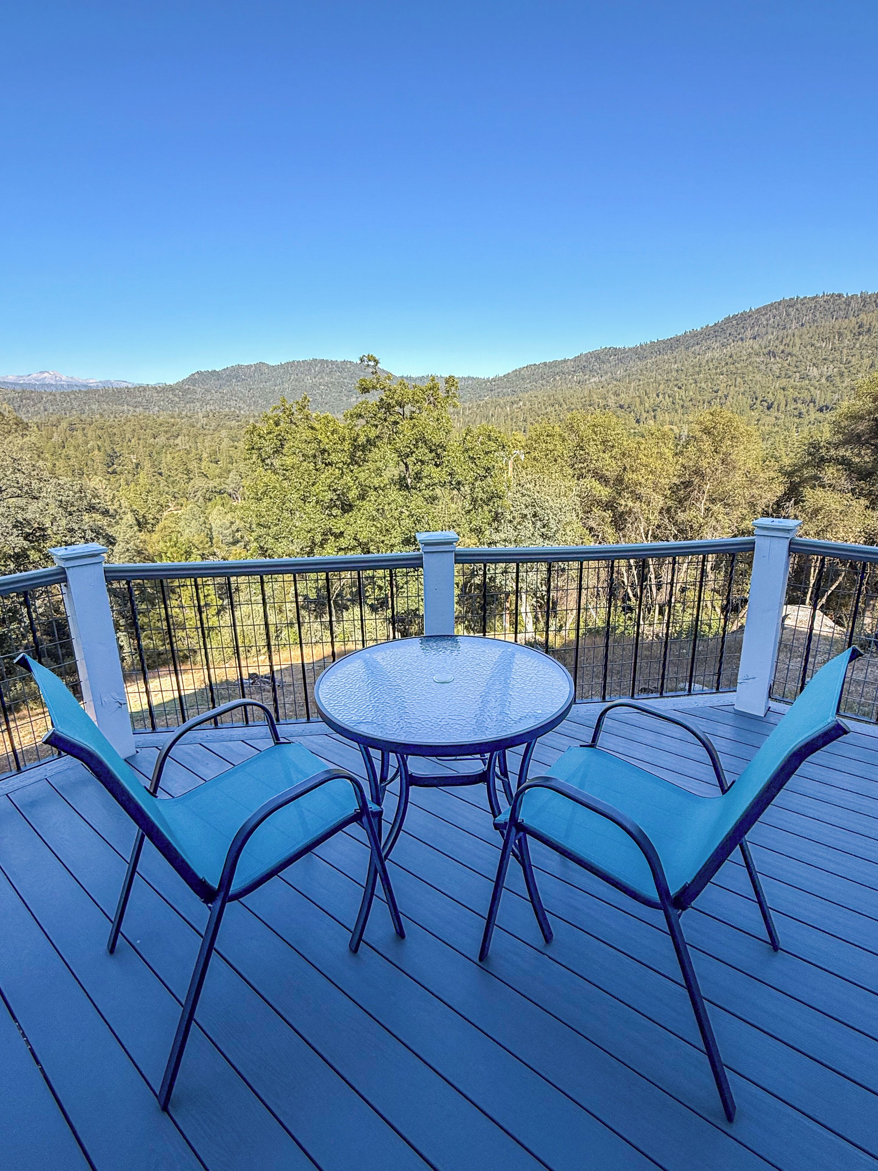 Une terrasse avec une table ronde et quatre chaises, offrant une vue sur une chaîne de montagnes boisée.