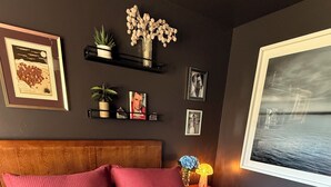 Un dormitorio con una cama grande, cabecera, mesita de noche con lámpara, y decoración de pared que incluye cuadros y un jarrón con flores.
