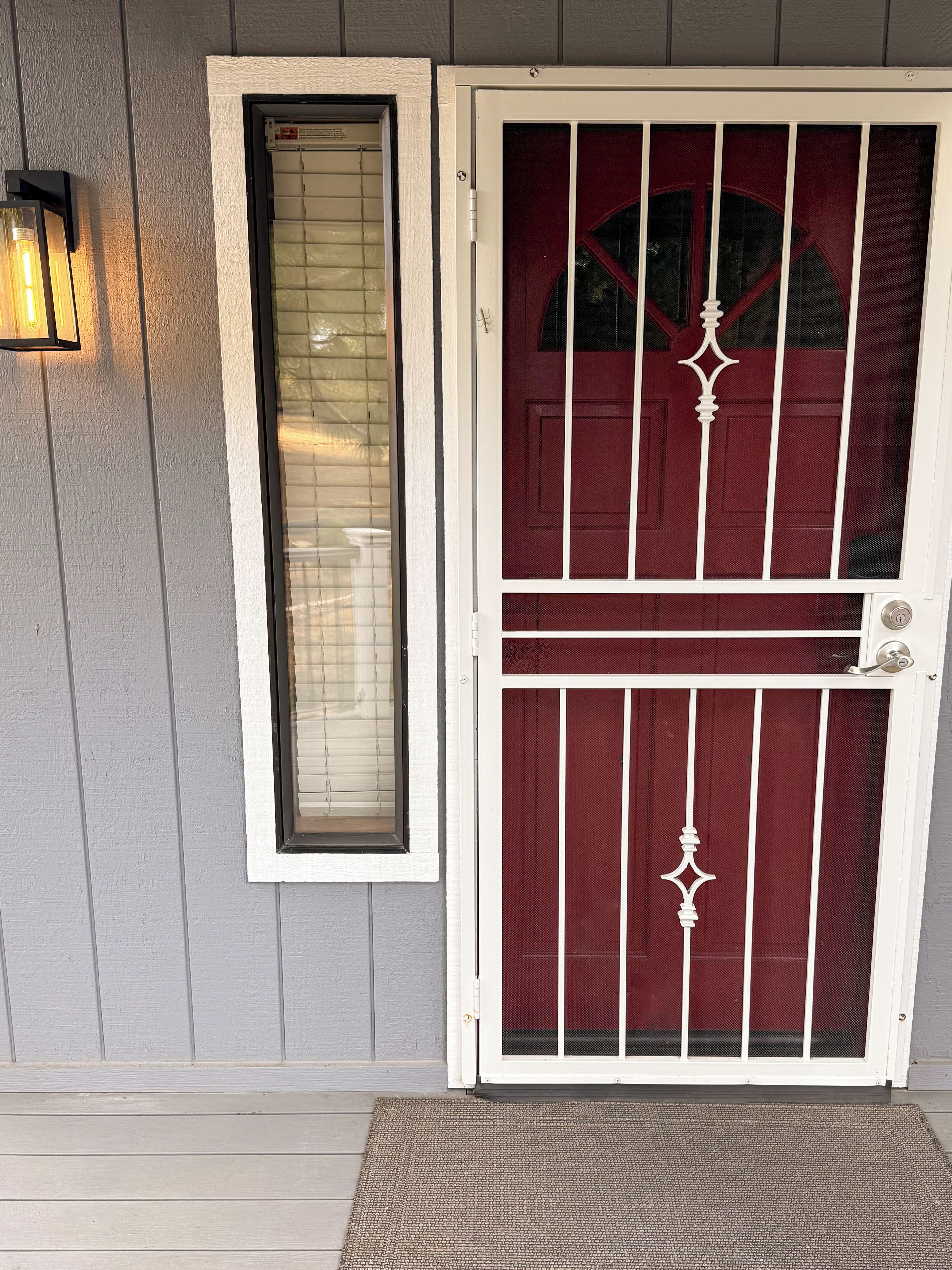 Una puerta blanca con un panel rojo y otro de cristal, una pared blanca y una lámpara.