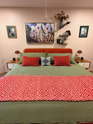 A bed with a patterned red and green bedspread, a green and red striped pillow, and a painting above the bed. - Mountain Daddies Bed & Breakfast (Oakhurst)