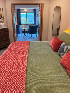 Un dormitorio con cama, cómoda, espejo y vista a un comedor con mesa y sillas.