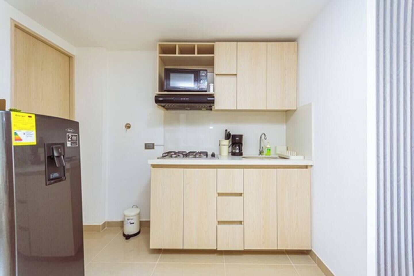 Eine kleine Küche mit Kühlschrank, Mikrowelle, Herd und Schränken.