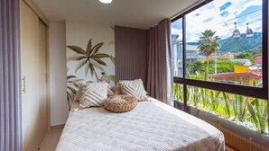 Une chambre avec une grande fenêtre, un lit recouvert d’une literie à motifs, et une vue sur un paysage montagneux.