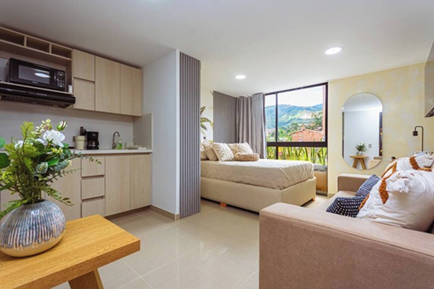 Una habitación moderna con cama, sofá, zona de cocina y un ventanal con vistas amplias.
