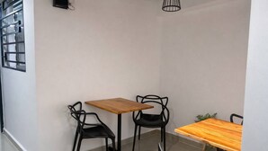 Une pièce d’angle avec deux tables et des chaises, une fenêtre avec des stores et un luminaire suspendu.