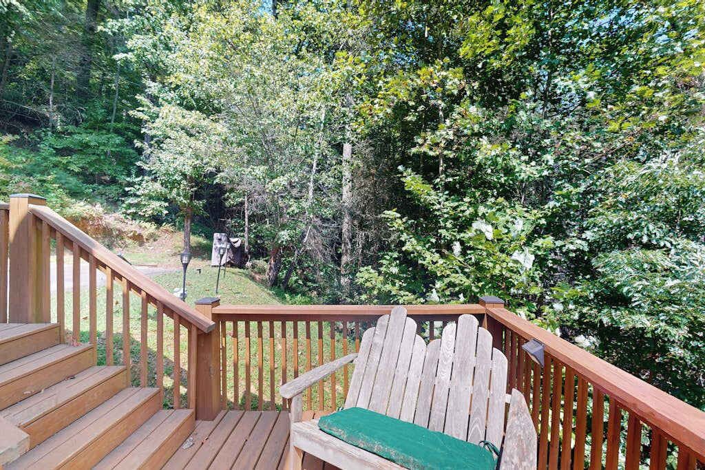 A wooden deck with a bench and stairs leading to a forested area.