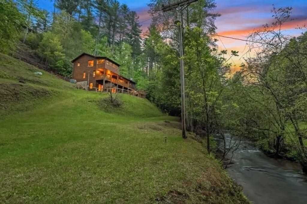 A wooden cabin with a balcony, surrounded by greenery and a river.