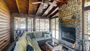 Ein rustikales Blockhaus-Interieur mit Kamin aus Stein, Holzbalkendecke und einer Couch mit Kissen.