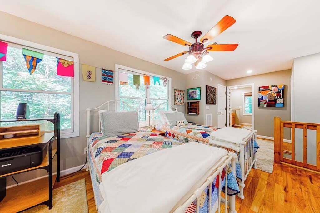 Une chambre avec deux lits, un ventilateur de plafond, un bureau et une fenêtre avec des rideaux.