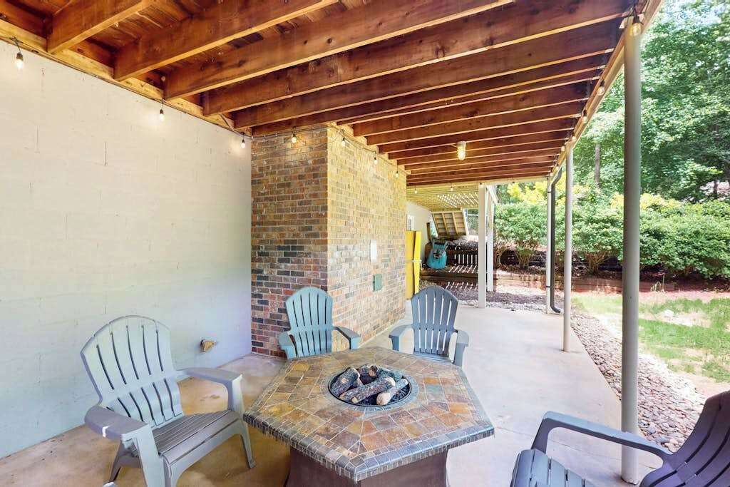 Un patio al aire libre con chimenea de ladrillo, vigas de techo de madera y sillas de colores claros.