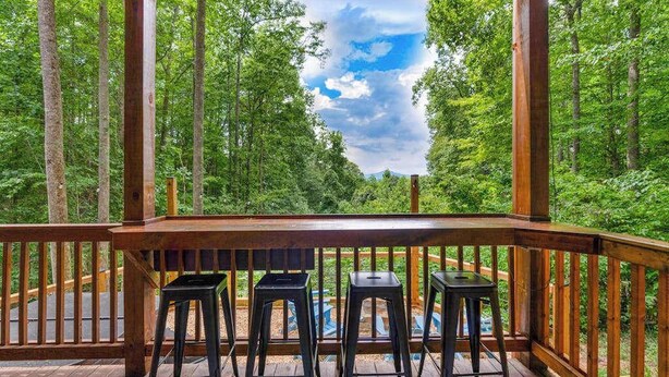 Eine Holzdar Terrasse mit Tisch und vier Hockstühlen, mit Blick auf ein bewaldetes Gebiet.