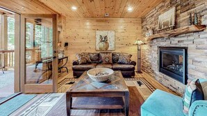 Ein Blockhaus-Interieur mit Kamin, Holzwänden, einer Couch und einem Esstisch.