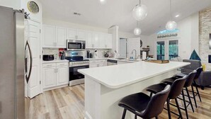 A modern kitchen with white cabinets, stainless steel appliances, a central island with bar stools, and pendant lighting. - Hawk’s Landing at Innsbruck (Helen)
