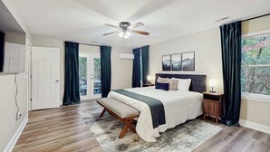 A bedroom with a bed, a bench, a ceiling fan, a nightstand, and a window with curtains. - Hawk’s Landing at Innsbruck (Helen)