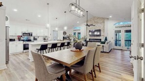 A spacious kitchen with white cabinets, a dining area with a wooden table and chairs, a ceiling fan, and a TV. - Hawk’s Landing at Innsbruck (Helen)