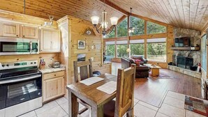 Interior de una cabaña de madera con cocina, comedor y chimenea.