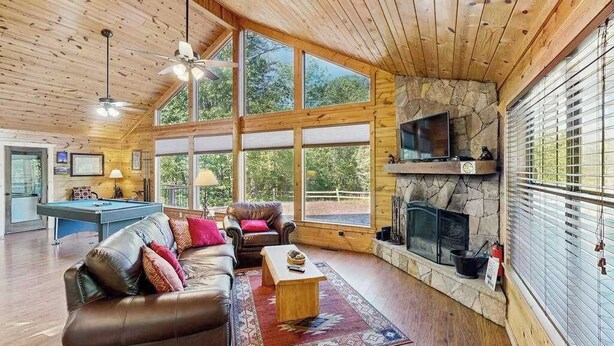 Un salón amplio con mesa de billar, sofá de cuero y chimenea de piedra.
