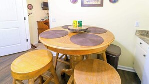 Una mesa redonda de madera para comer con cuatro taburetes, un estante pequeño con dos recipientes y un cubo de basura.