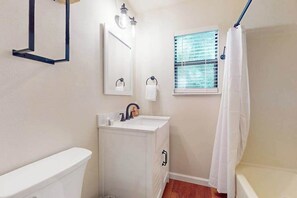 A bathroom with a toilet, sink, mirror, and window with blinds. - Poppys Farmhouse Cabin (Blue Ridge)
