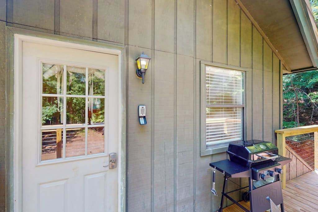A wooden deck with a grill, a white door, and a window with blinds.