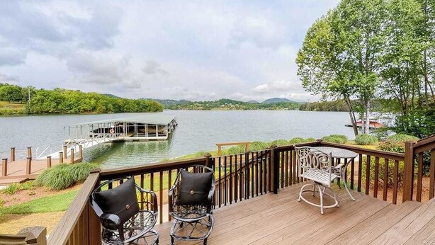 A deck with chairs overlooking a lake, a dock, and a forested area. - Lake Chatuge Retreat (Hiawassee)