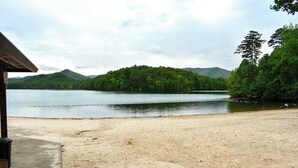 A beach with a sandy shore, a wooden structure, and a lake surrounded by forested hills. - Lake Chatuge Retreat (Hiawassee)