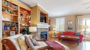 A living room with a fireplace, a red sofa, a wooden bookshelf, and a television. - Lake Chatuge Retreat (Hiawassee)