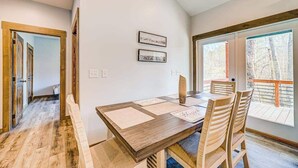 A dining area with a wooden table and chairs, framed pictures on the wall, and a view of the outdoors through large windows. - Hardwood Hideaway Stay (Ellijay)
