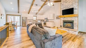 A spacious living area with a sofa, a fireplace, and a kitchen in the background. - Hardwood Hideaway Stay (Ellijay)