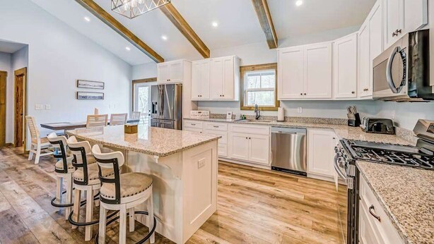 A spacious kitchen with white cabinets, a granite countertop, a central island with bar stools, a stainless steel refrigerator, and a gas stove. - Hardwood Hideaway Stay (Ellijay)