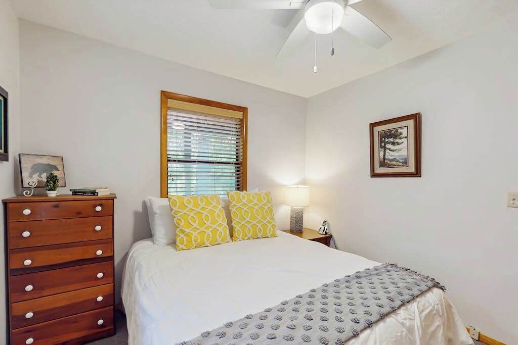 A bedroom with a bed, a dresser, a window with blinds, a ceiling fan, and a framed picture on the wall.