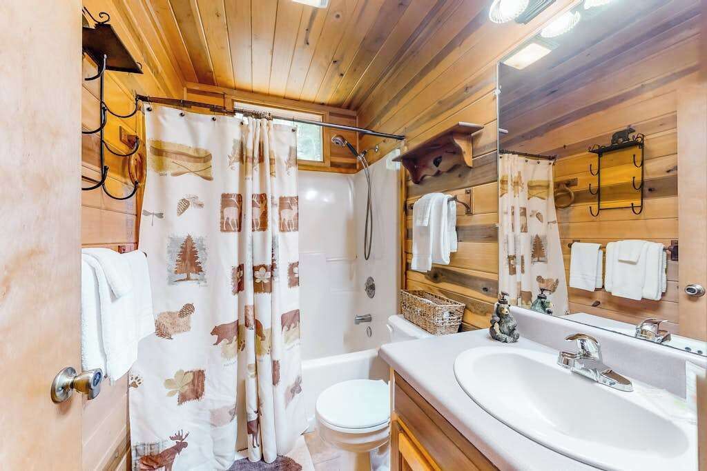 Een badkamer met douchegordijn, toilet, wastafel en spiegel.
