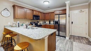A kitchen with wooden cabinets, a stainless steel refrigerator, a granite countertop, and a microwave. - Riverside Bears Den - Central Location (Helen)