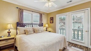 A bedroom with a bed, two bedside tables with lamps, a ceiling fan, and a door with a balcony. - Riverside Bears Den - Central Location (Helen)