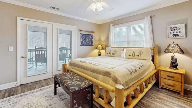 A bedroom with a bed, a ceiling fan, a bench, a nightstand, and a window with curtains. - Riverside Bears Den - Central Location (Helen)