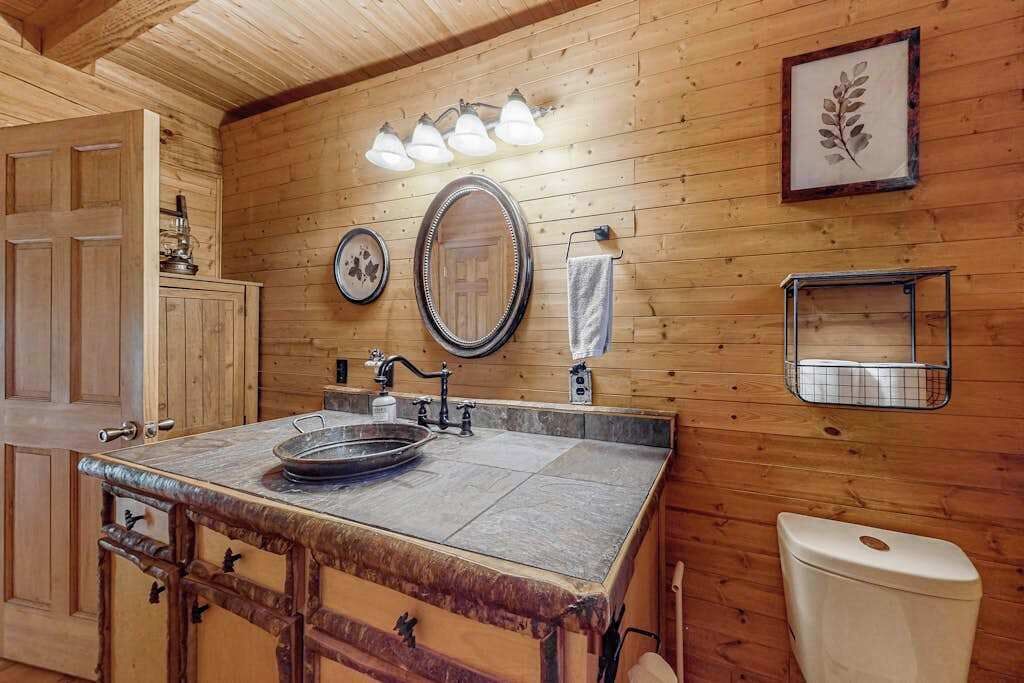 A wooden cabin interior with a kitchen area featuring a sink, a mirror, and a light fixture.