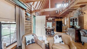 A log cabin interior with leather chairs, a dining table, and a kitchen area.