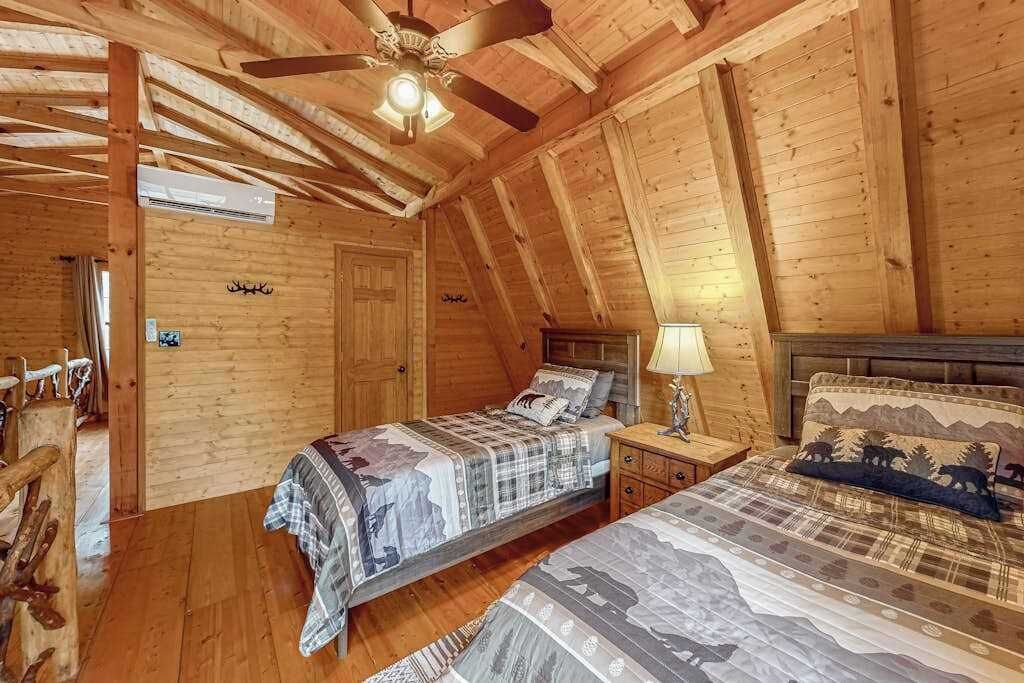 Camera da letto in una baita di legno con due letti, un ventilatore a soffitto e pavimento in legno.