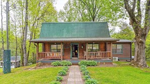 A log cabin with a porch, a front door, and a pathway leading to the entrance.
