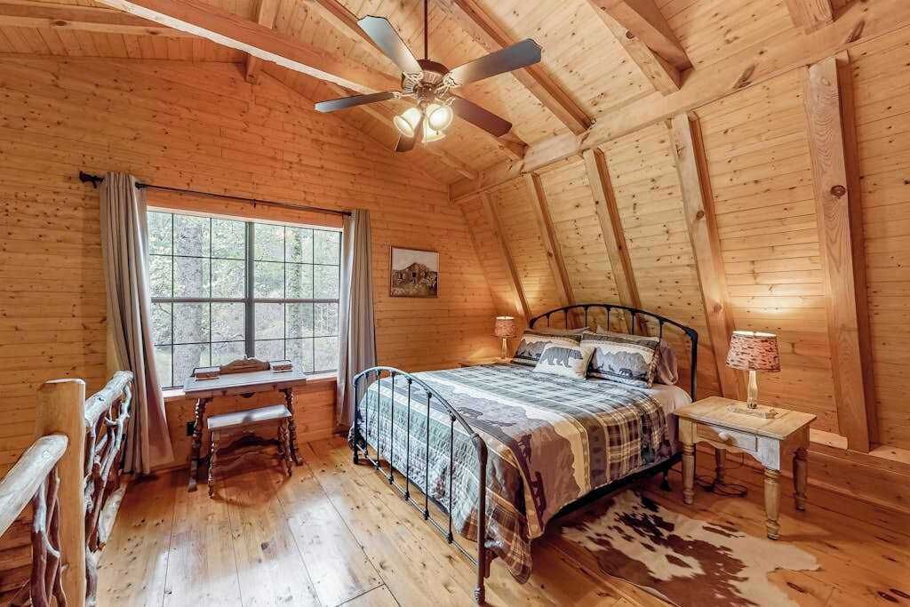 Een slaapkamer in een blokhut met een bed, bureau en raam.