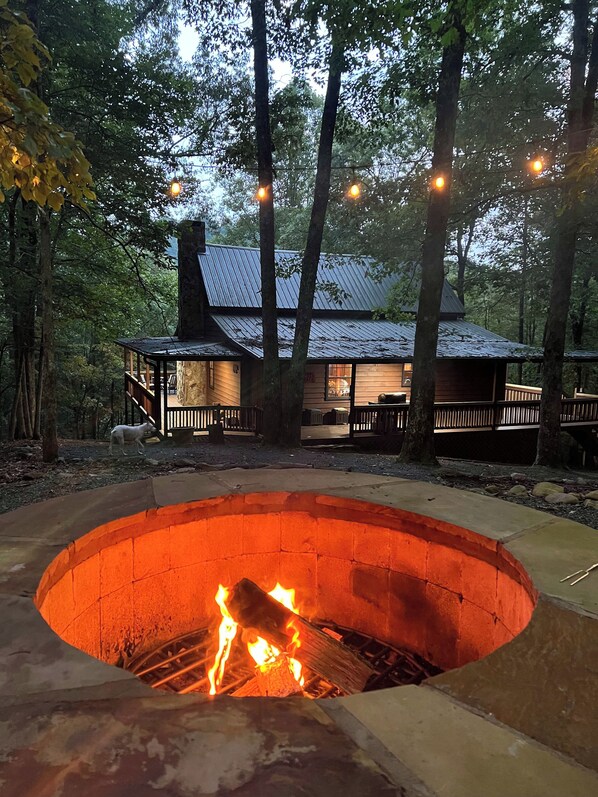 Ein rundes Feuerbecken im Freien mit brennendem Feuer, umgeben von einer Holzterrasse und Bäumen.