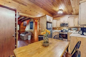 A wooden interior with a dining table, kitchen area, and a living space with a sofa and a fireplace. - Dream in the Bluff Cabin (Mineral Bluff)