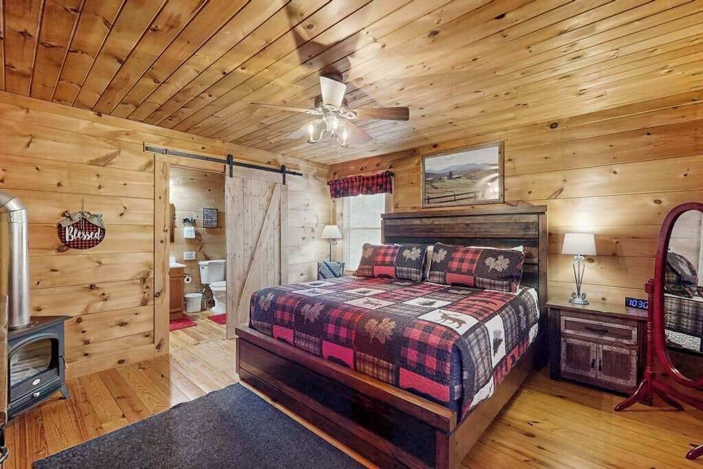 A wooden cabin bedroom with a bed, a ceiling fan, a fireplace, and a rustic decor.